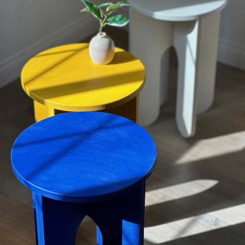 Colorful side tables in blue, yellow, and white, ideal for use as a table, seat, or plant stand.