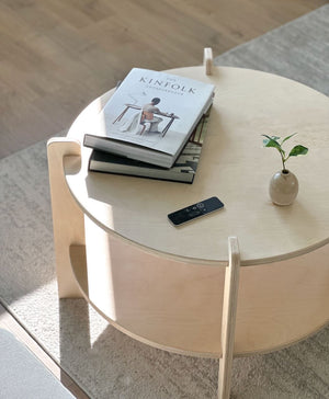 Stylish round coffee table with books, a remote, and a small plant accenting a modern living room.