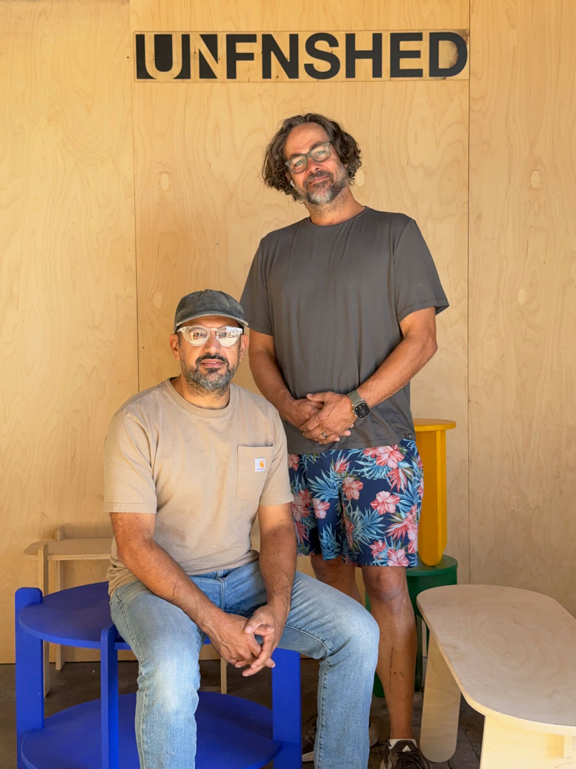 Two creators in the UNFNSHED workshop with colorful furniture pieces and a sign that says UNFNSHED
