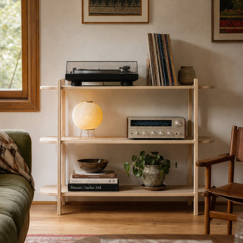 A light natural wood open shelving unit styled in a cozy living room setting, holding a turntable, records, a glowing globe lamp, books, and a small potted plant.