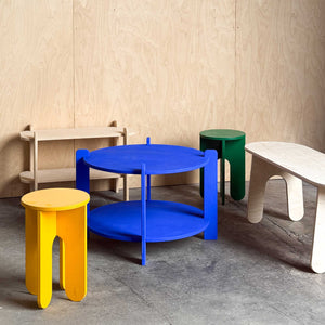 Colorful round coffee table in blue surrounded by various modern tables in yellow, green, and natural wood.