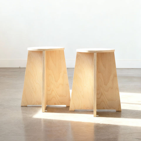 Two wooden stools with a minimalist design on a reflective floor.