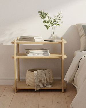 Wooden night stand with books and a plant next to a bed in a bedroom setting