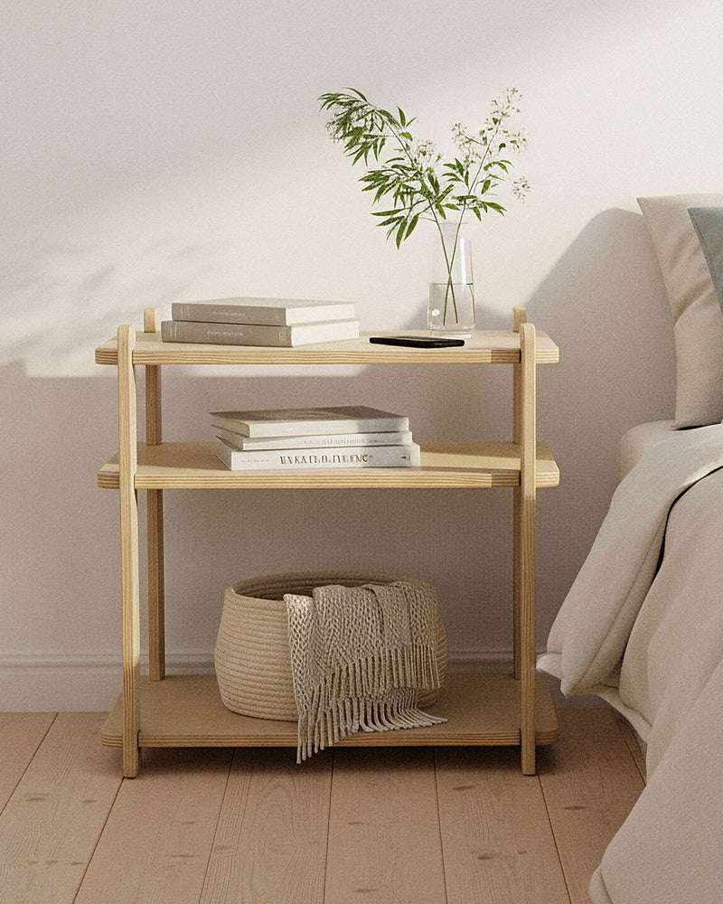 Wooden night stand with books and a plant next to a bed in a bedroom setting