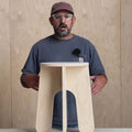 Person demonstrating the No Tool Stool, a versatile unfinished stool that requires no tools for assembly.