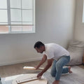 Man assembling a round coffee table on a rug in a bright living room, showcasing easy setup and stylish design.