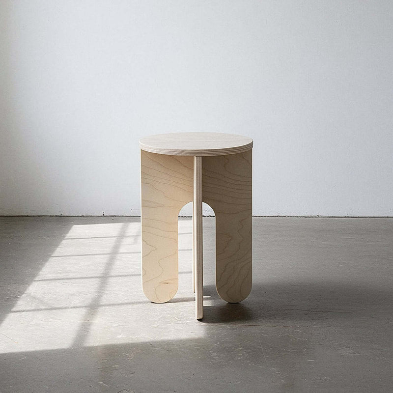 Round side table in a warehouse setting showing natural Baltic birch finish